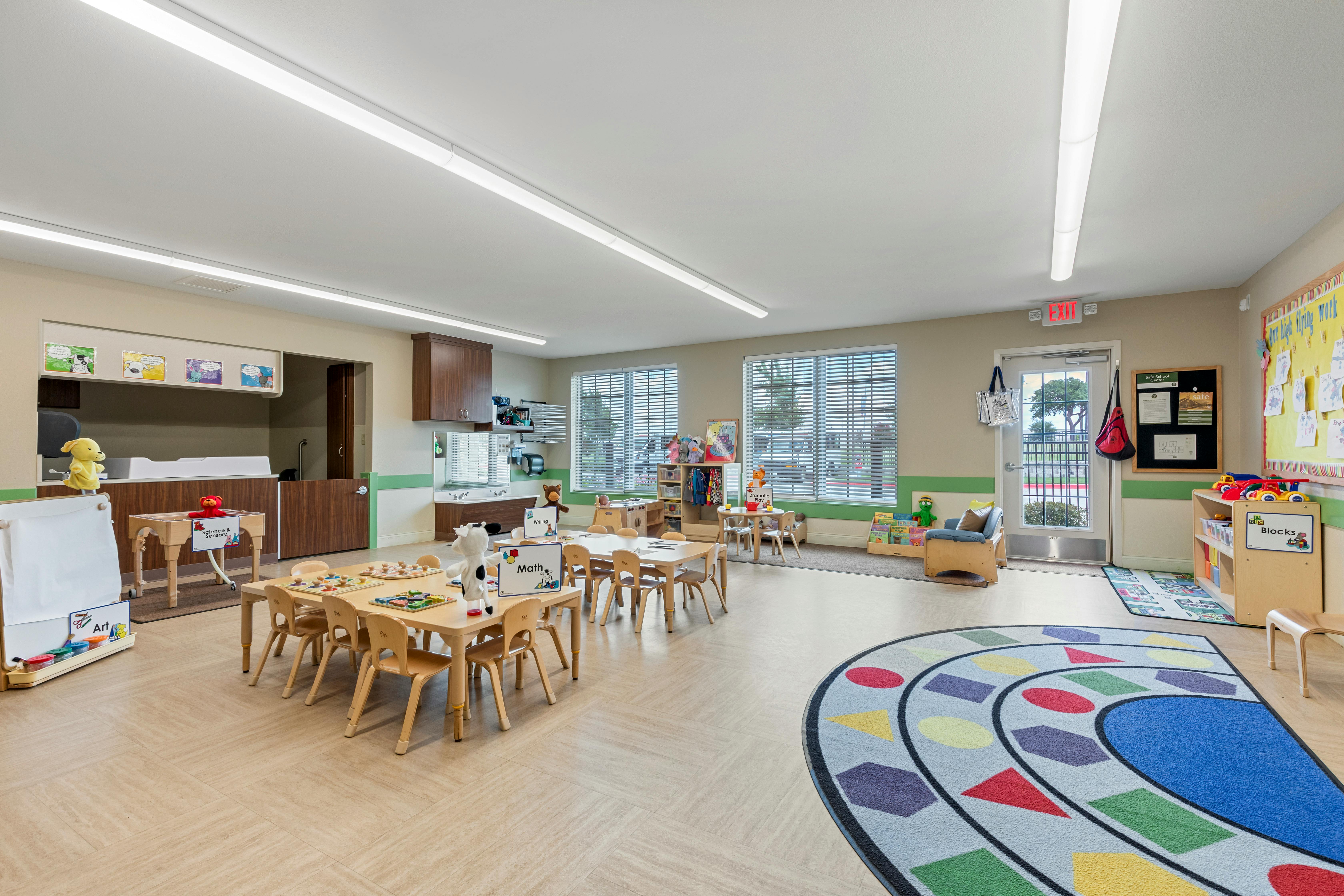Classroom with small tables and chairs, a play rug, and activity areas