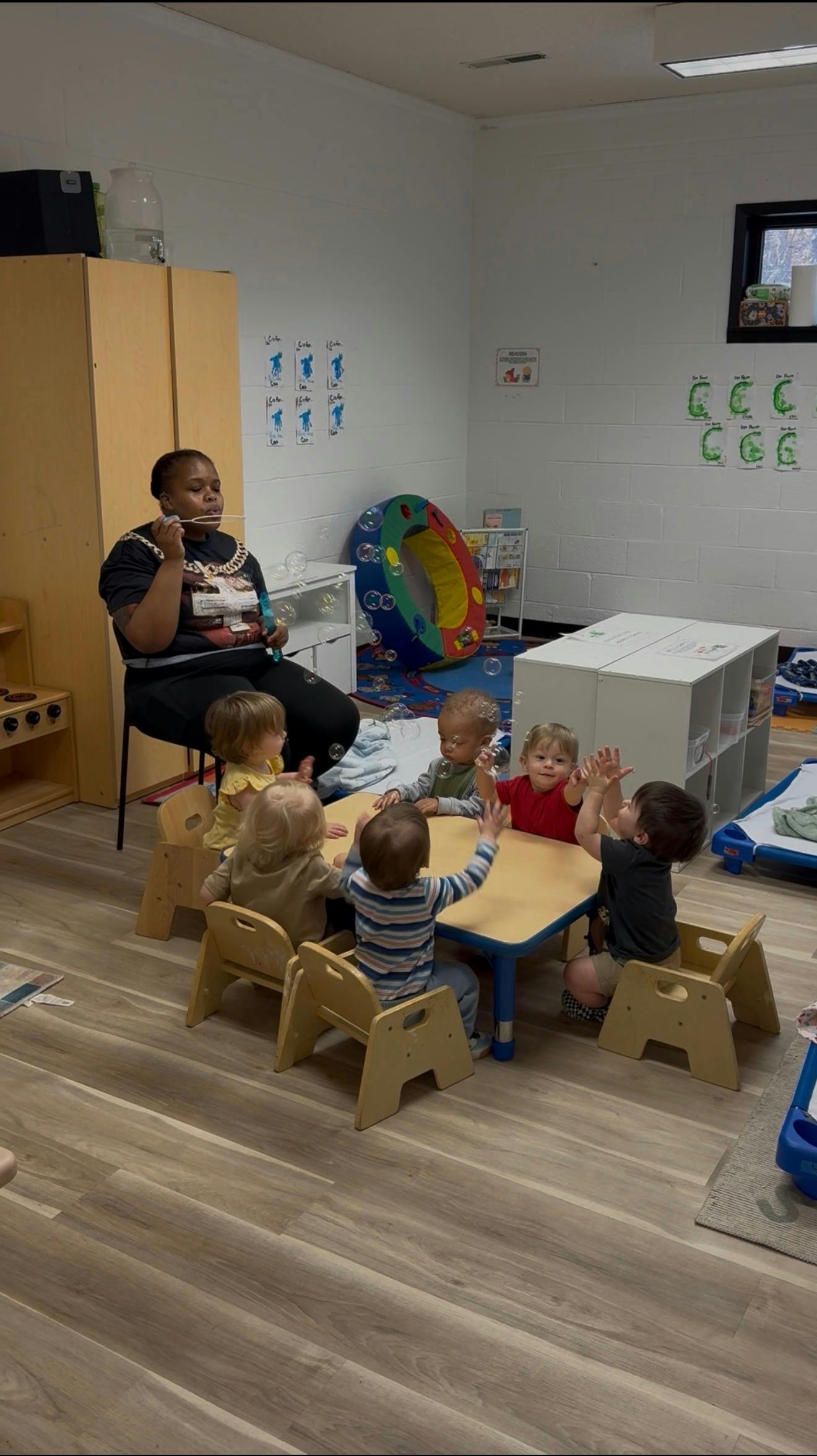 A person blowing bubbles for children sitting at a table in a classroom
