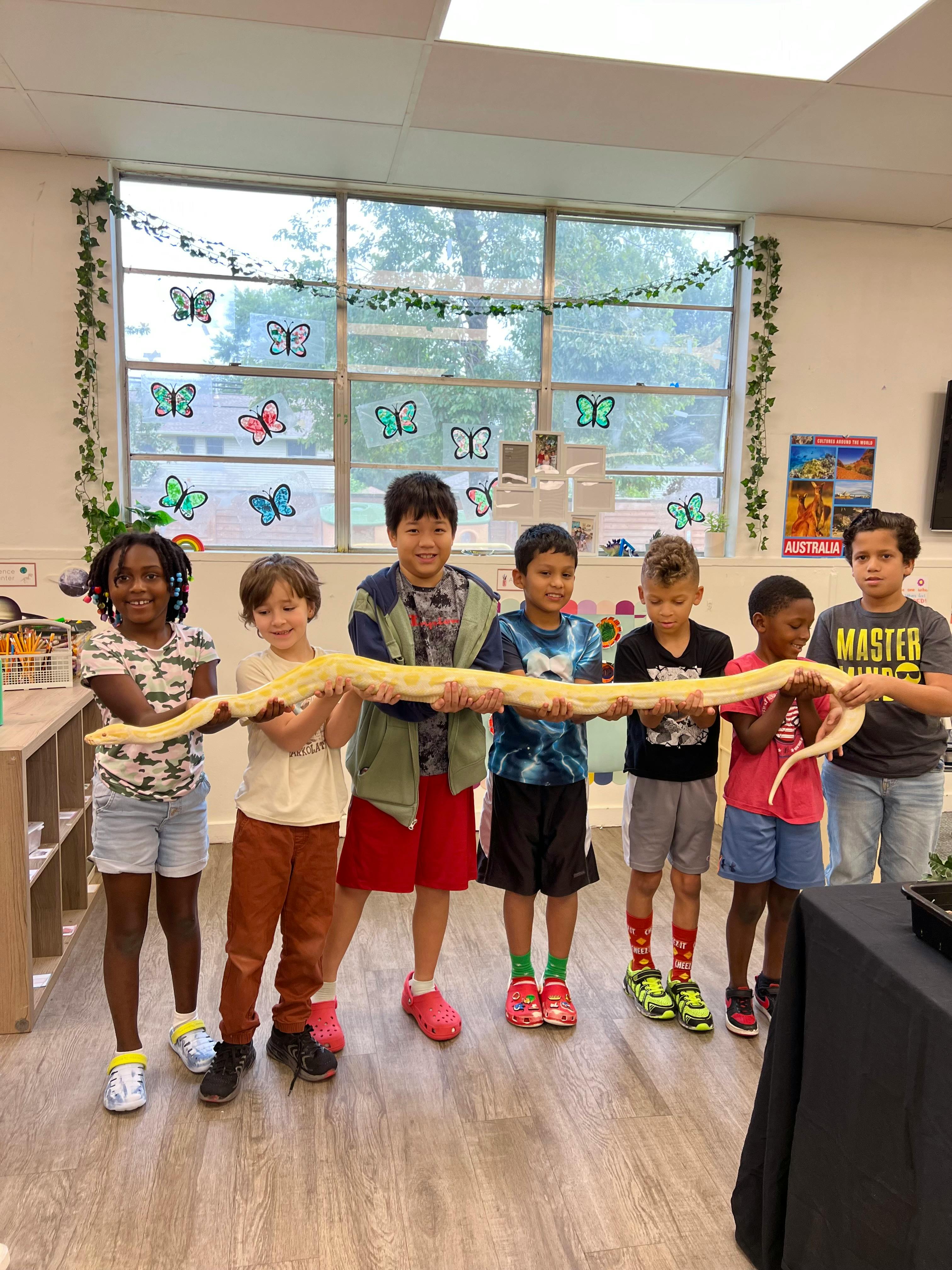 Six children holding a large snake in a classroom