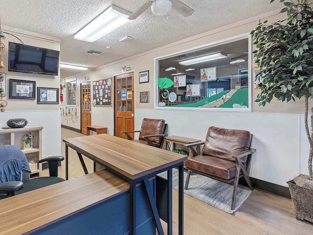 Reception area with a desk, two brown chairs, and a large window looking into a hallway
