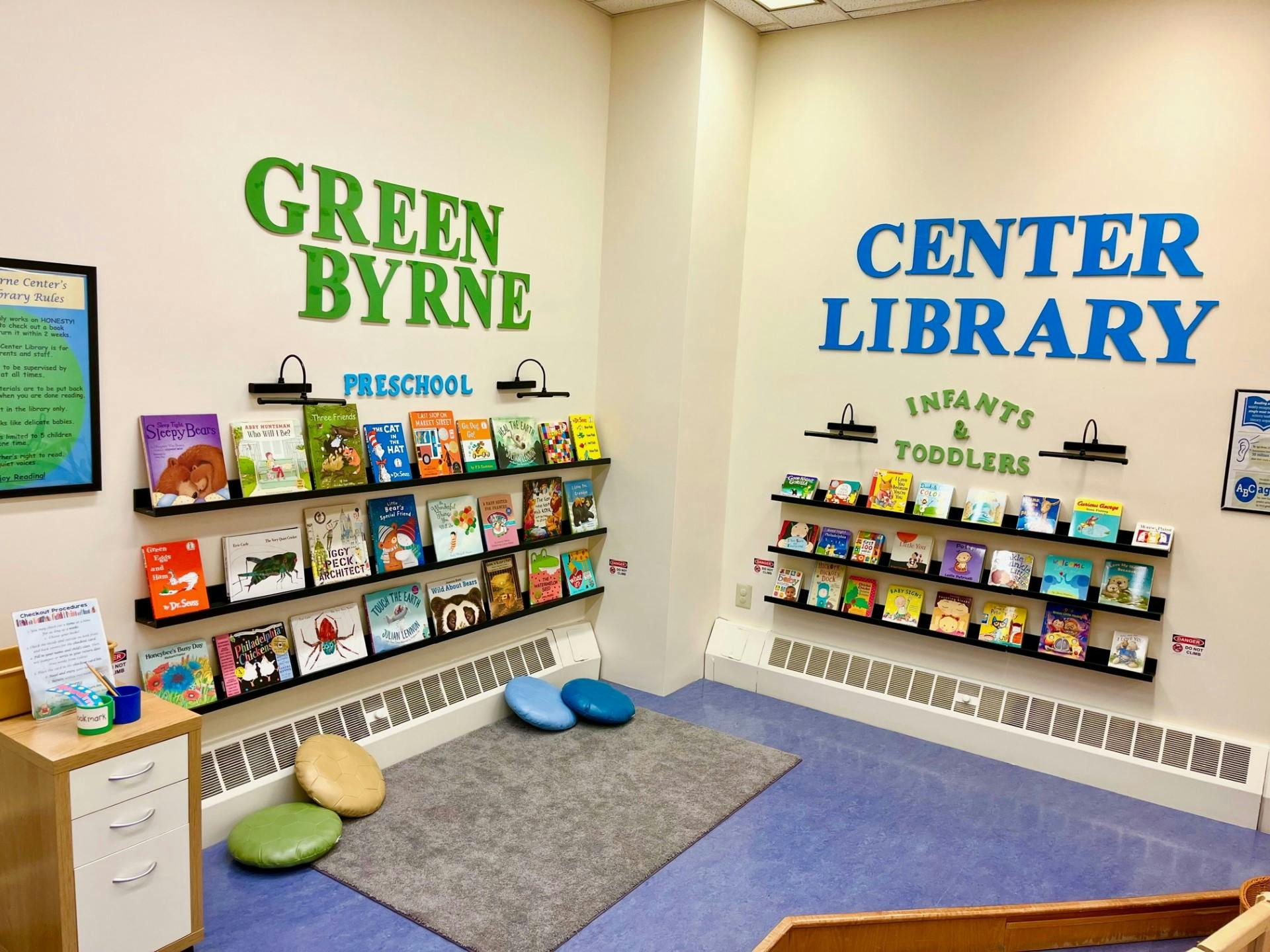 Library room with low bookshelves filled with children's books and cushions on the floor