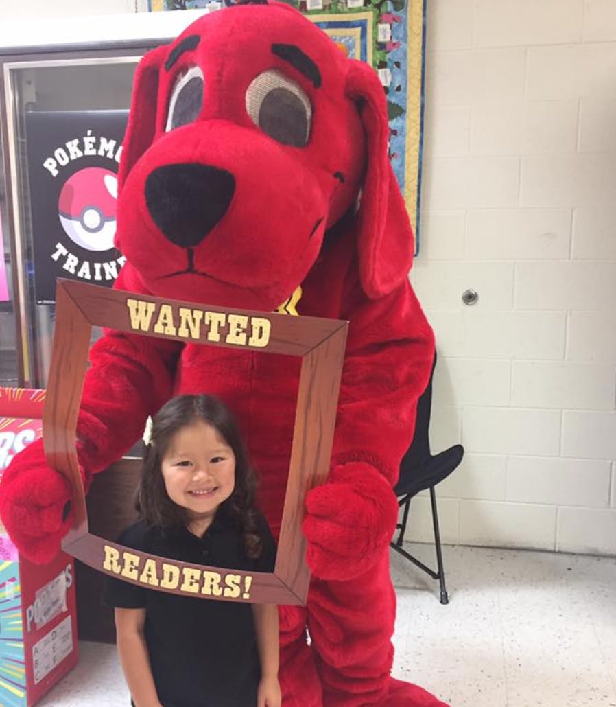 Red dog mascot and child holding a "Wanted Readers!" sign