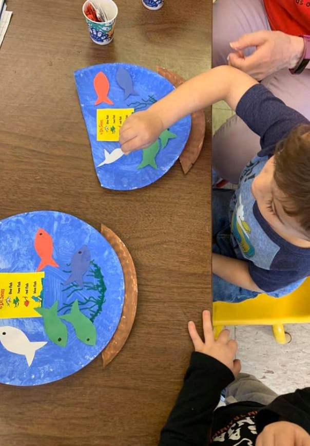 Child working on a paper plate craft with fish cutouts