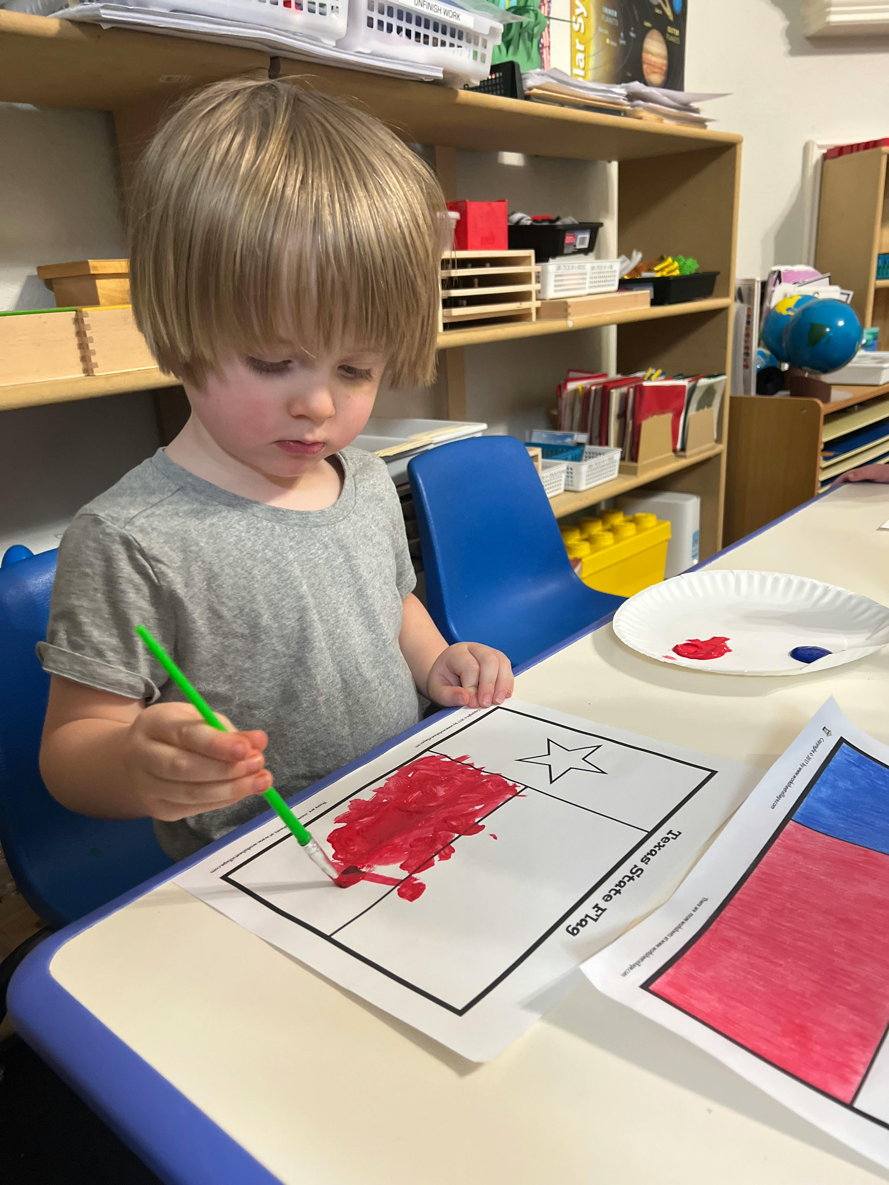 Child painting a flag outline with red paint