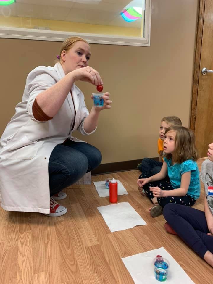 Person in lab coat demonstrating experiment to children
