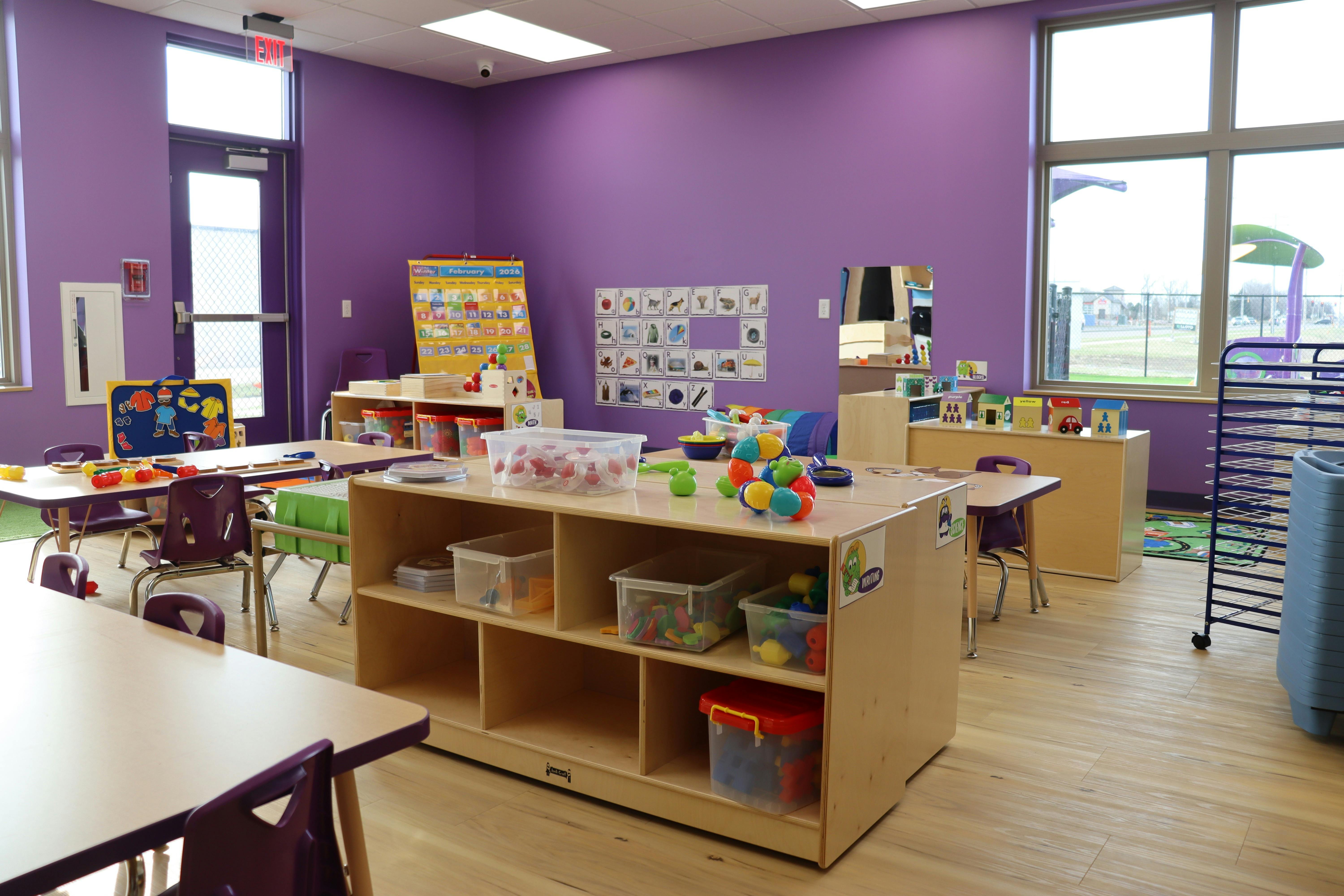 A classroom with purple walls, small tables, chairs, and learning materials