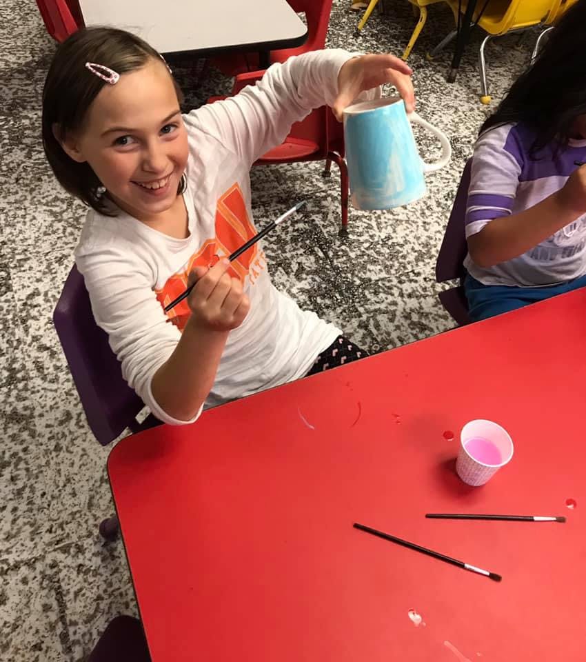 Child holding a paintbrush and a painted mug