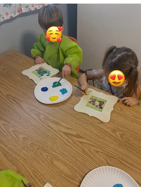 Two children painting wooden frames at a table