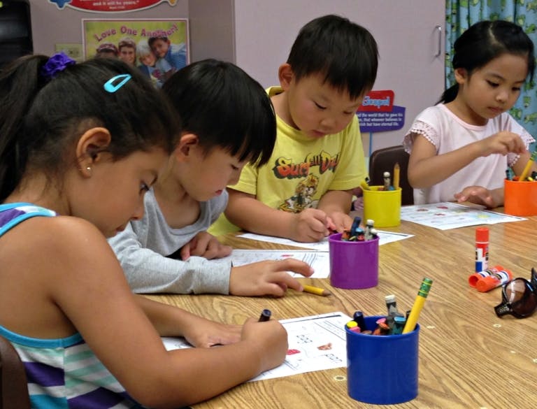 Four children drawing and coloring at a table