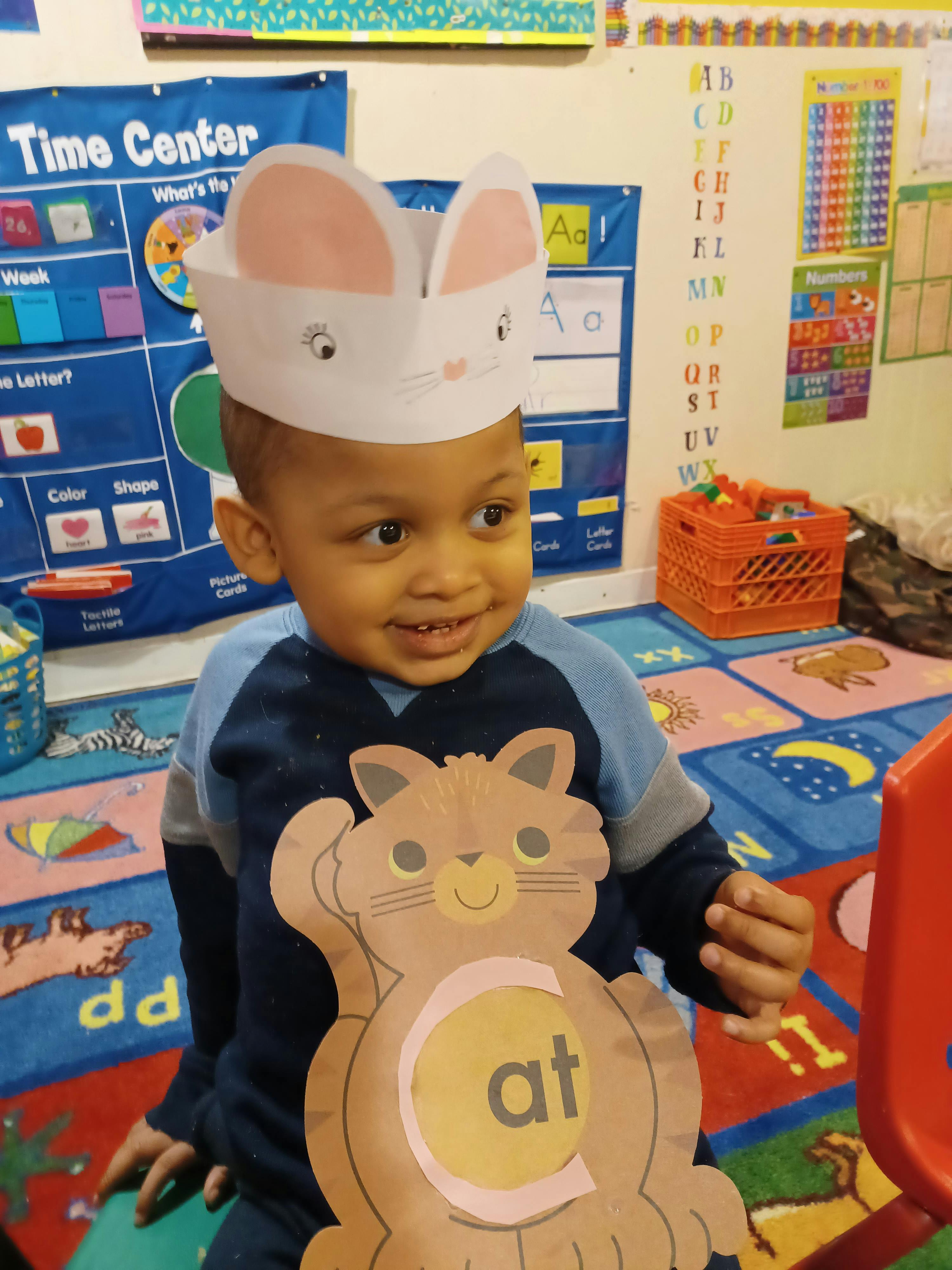 Child wearing a bunny hat and holding a cat cutout with "at" on it