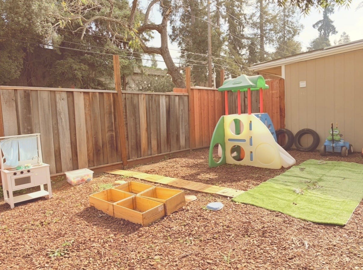 Child's backyard play area with playhouse, wooden boxes, and wood chips