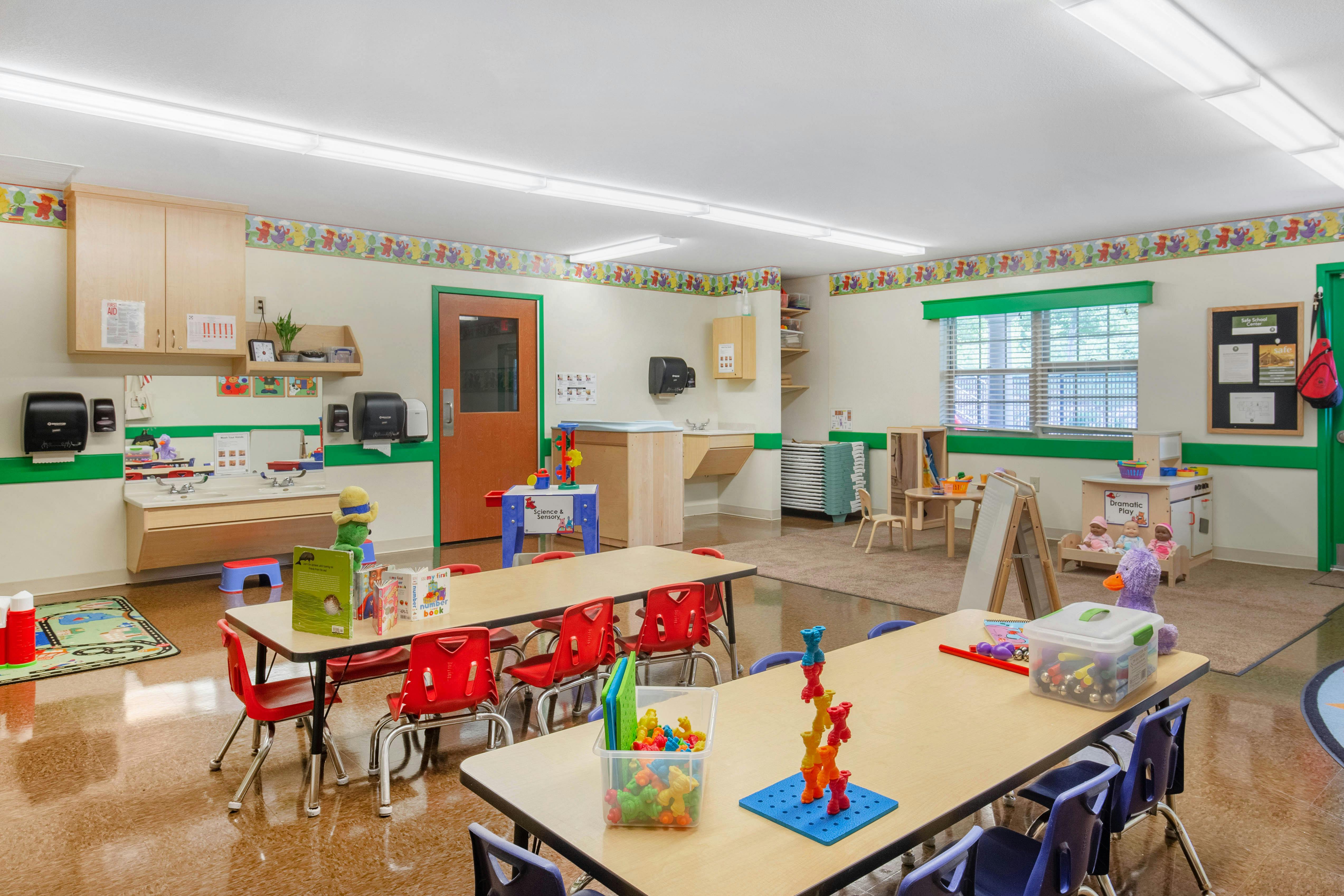 Classroom with child-sized tables and chairs, play areas, and sinks