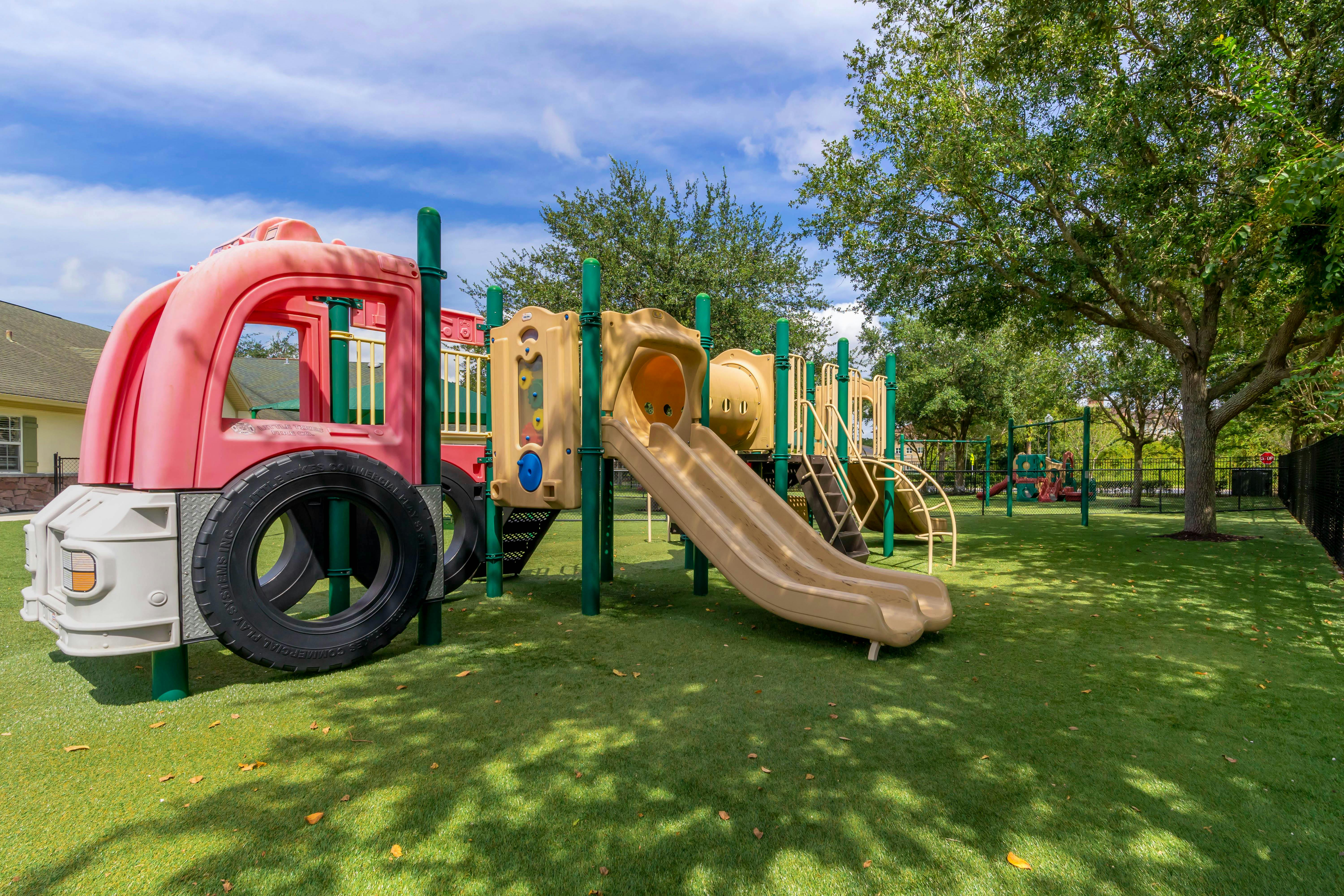 Playground with red truck-shaped structure, slides, and stairs on artificial grass