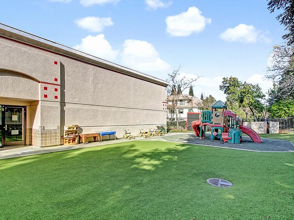 Outdoor playground with artificial turf, building, and play structure with slides