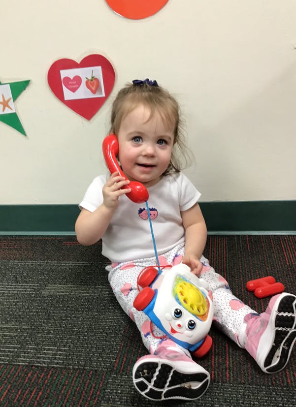 Child sitting on floor holding a toy telephone to their ear
