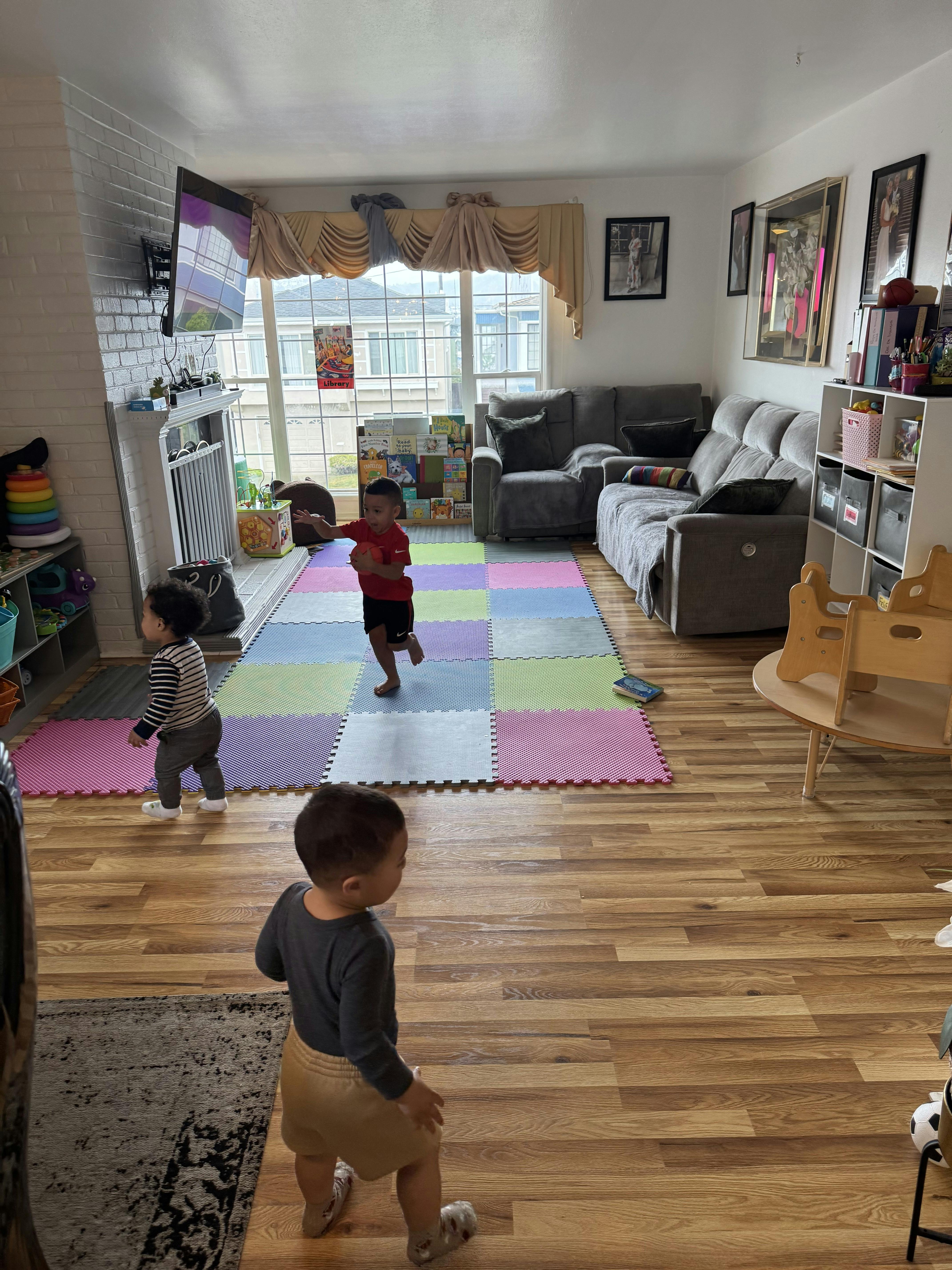 Three children playing on a colorful mat in a living room