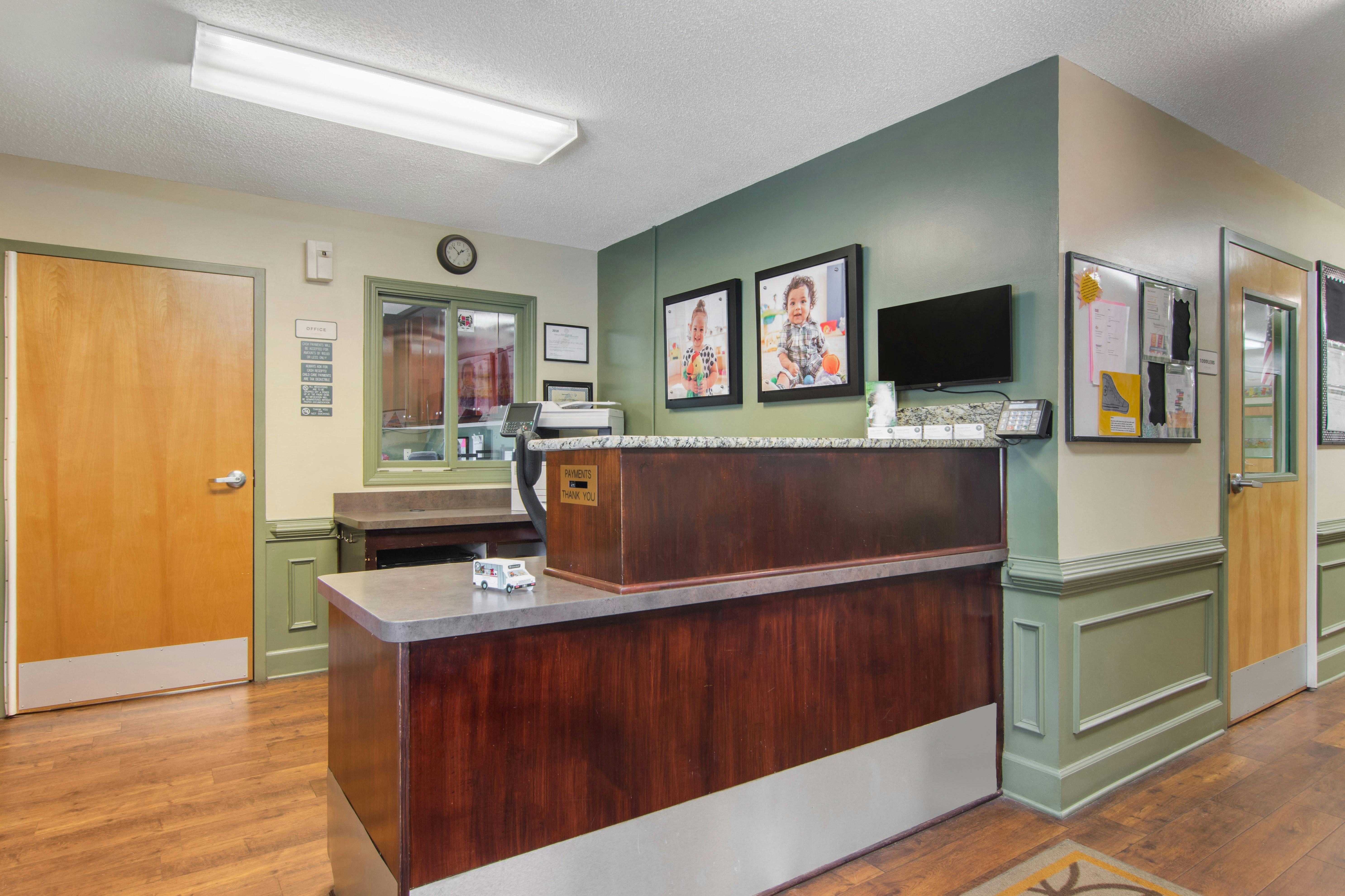 Reception area with a wooden counter, green walls, and framed pictures of children