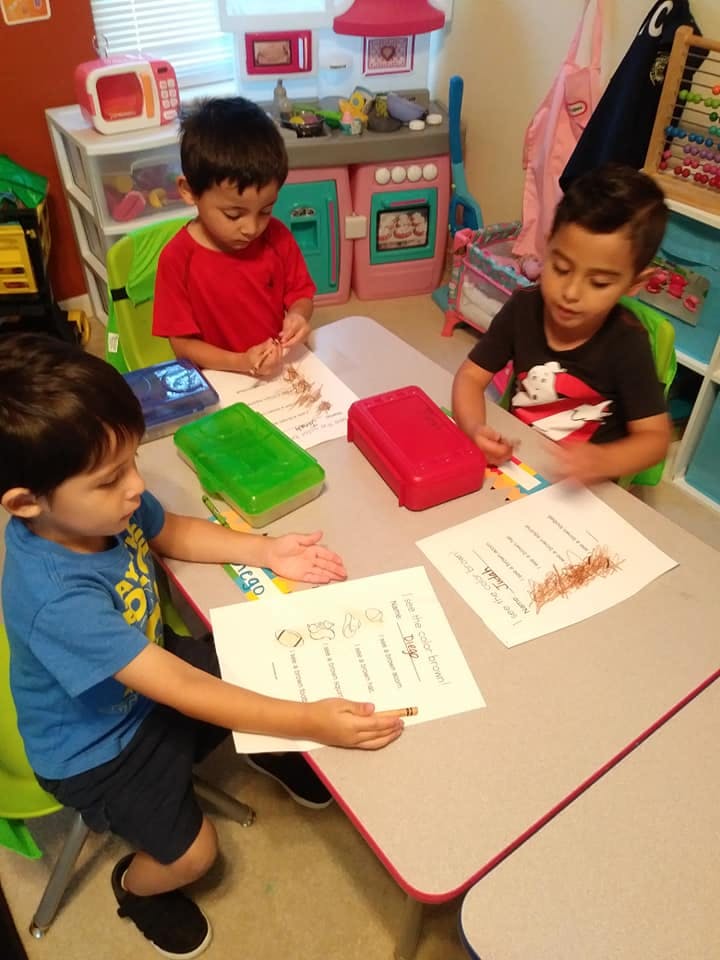 Three children sitting at a table with papers and art supplies