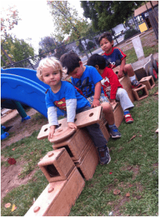Four children playing on a wooden train structure outdoors