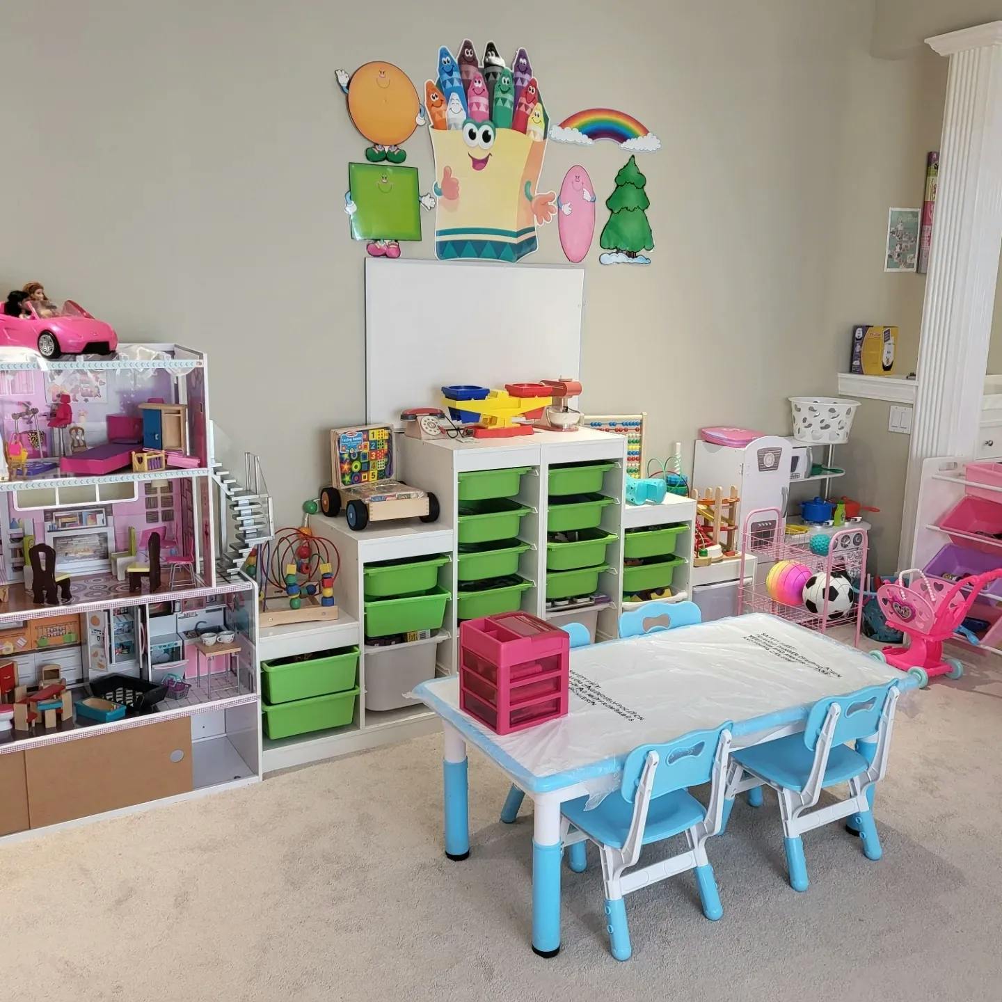 Playroom with a dollhouse, storage units with green bins, and a child-sized table and chairs