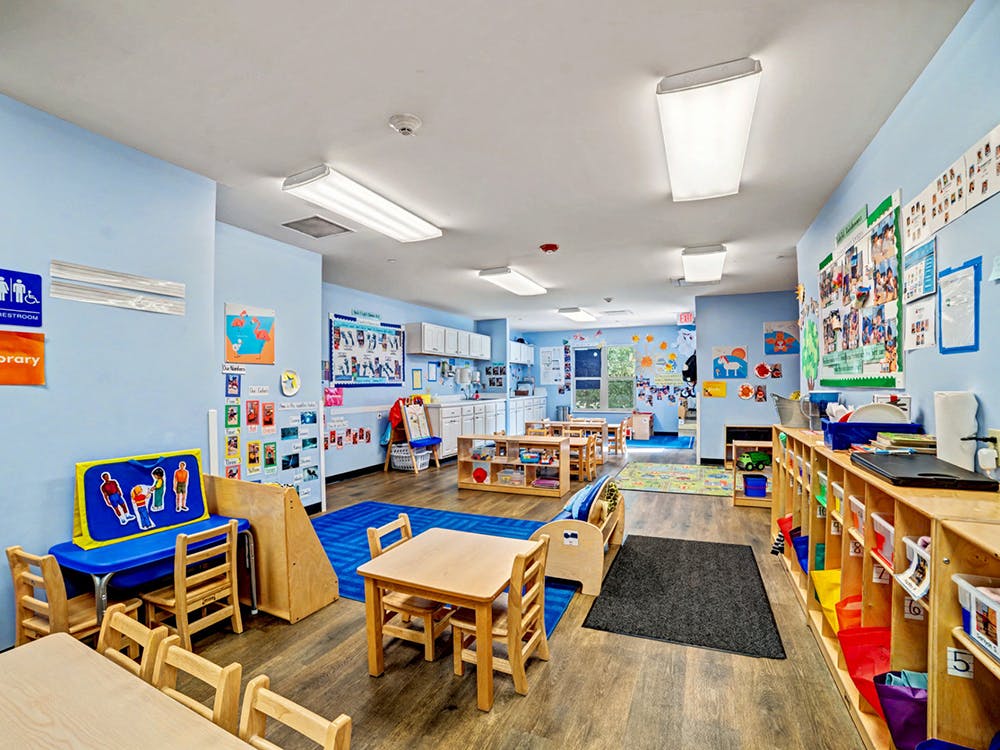 Classroom with children's tables and chairs, shelves, and art on light blue walls