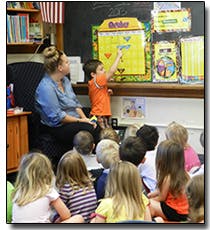 Adult and children in a classroom, child points to a calendar