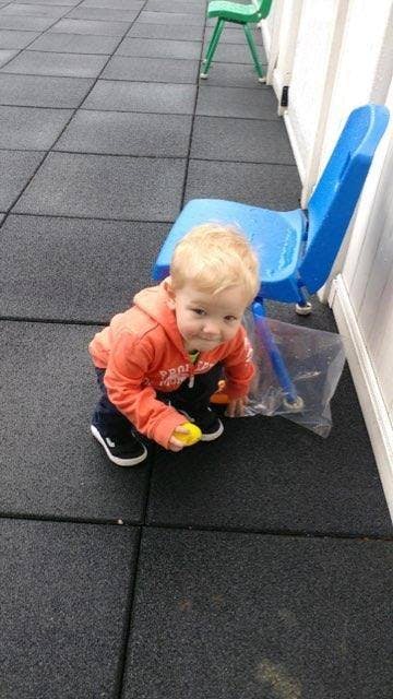 Child in orange hoodie crouching on a dark tiled floor