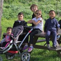 Four children and one adult sitting on a picnic table next to a stroller
