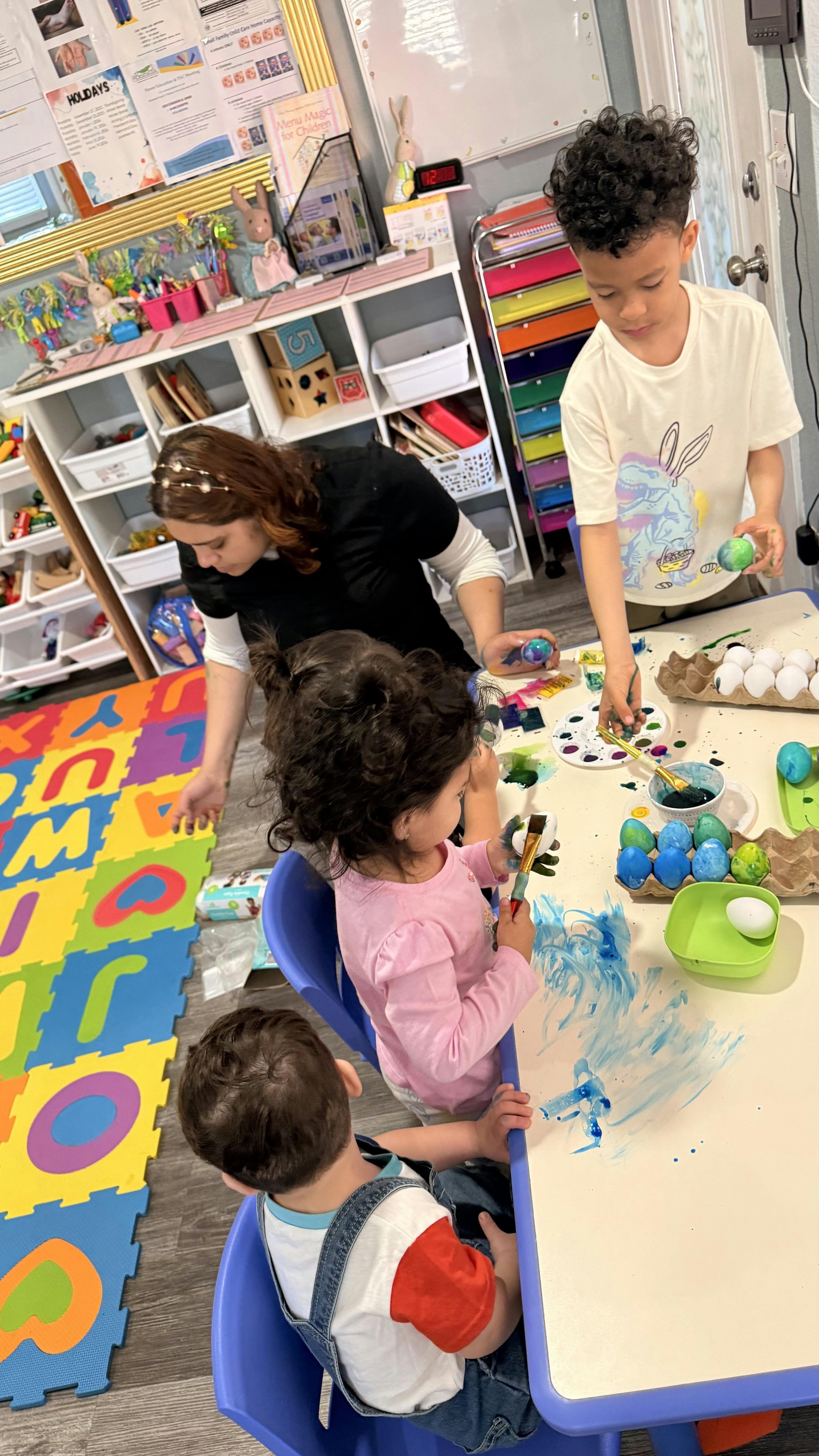 Adult and three children painting Easter eggs and making art at a table