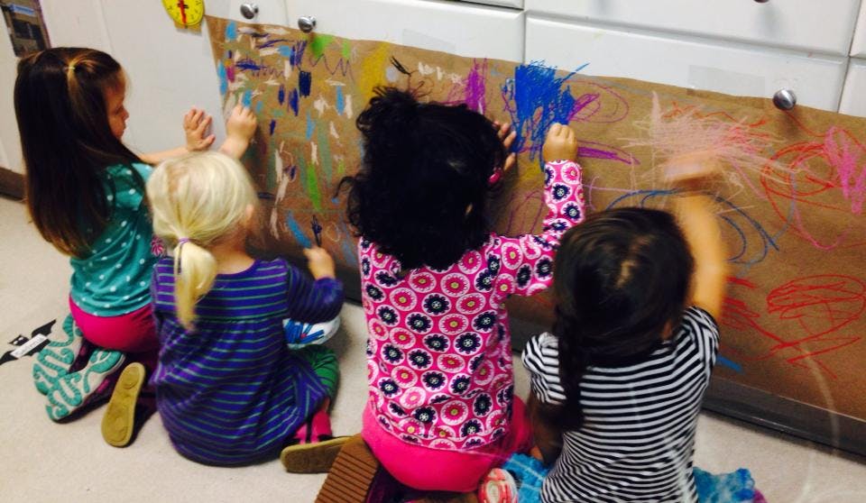 Four children painting on a large piece of paper