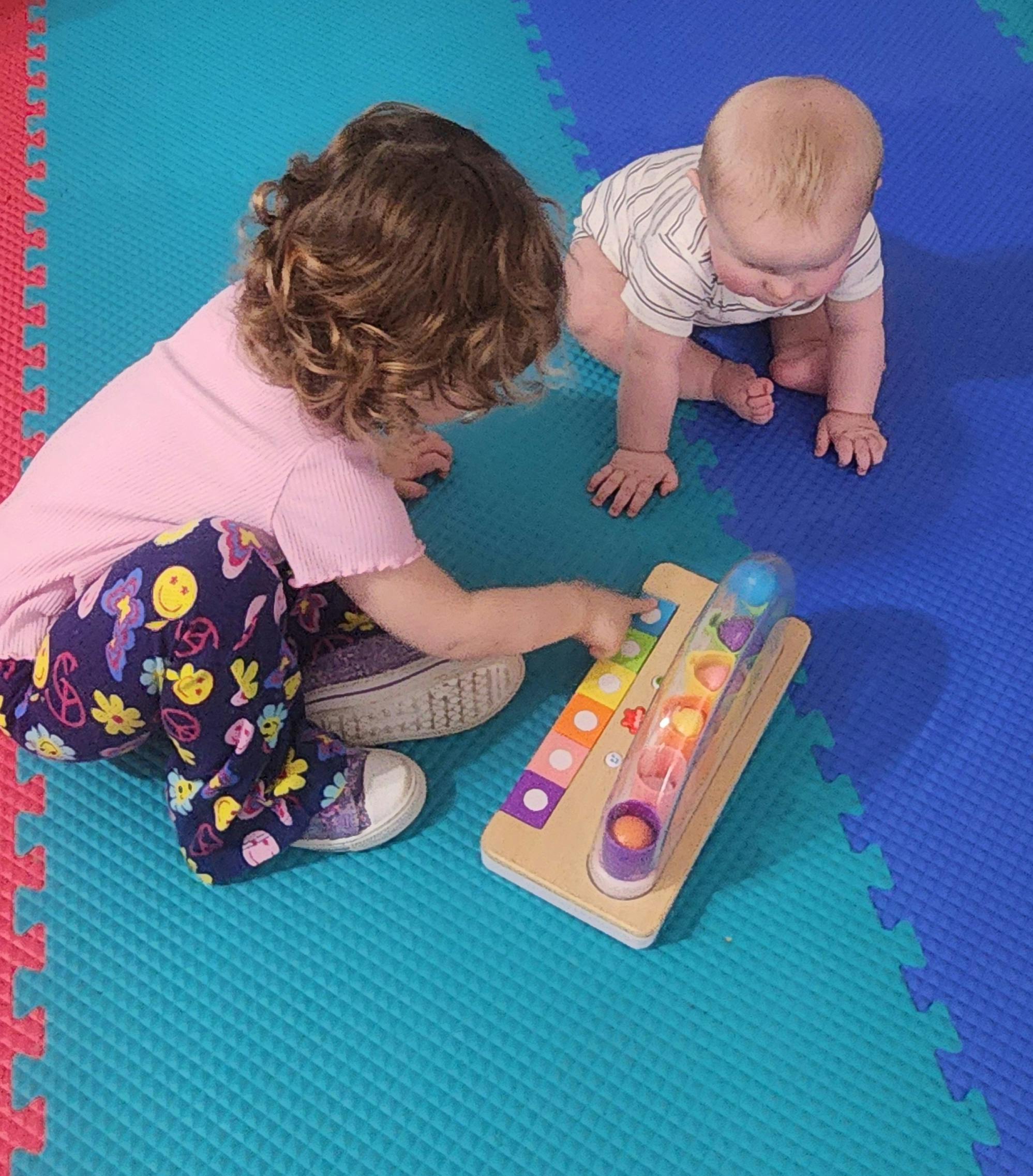 Child playing with a toy while a baby crawls nearby