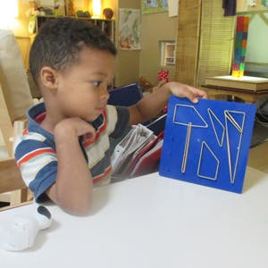 Child holding a blue geoboard with rubber bands forming shapes