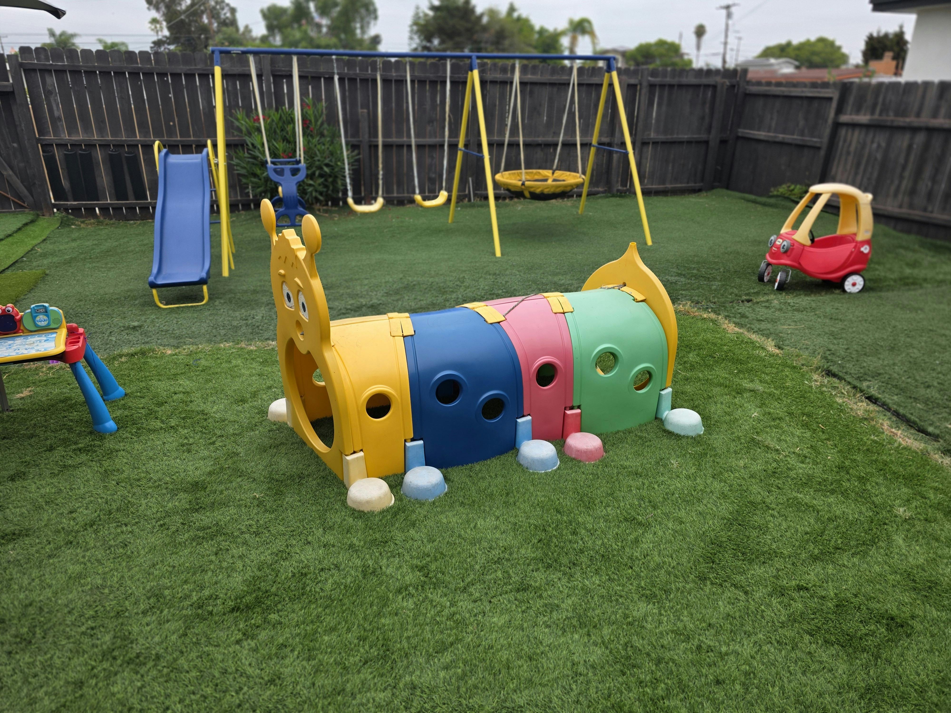 Playground with swings, slide, and caterpillar tunnel on grass