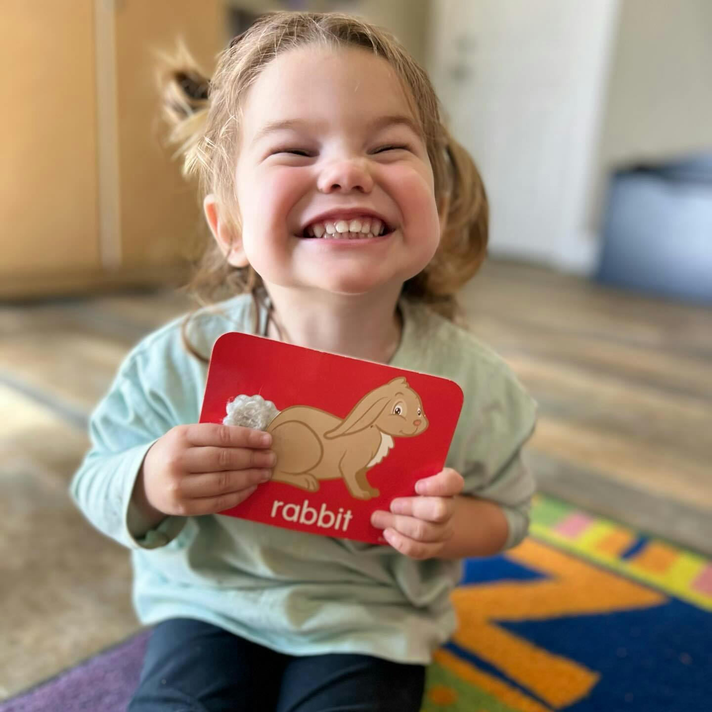 Child holding a red flashcard with a rabbit illustration and the word "rabbit"