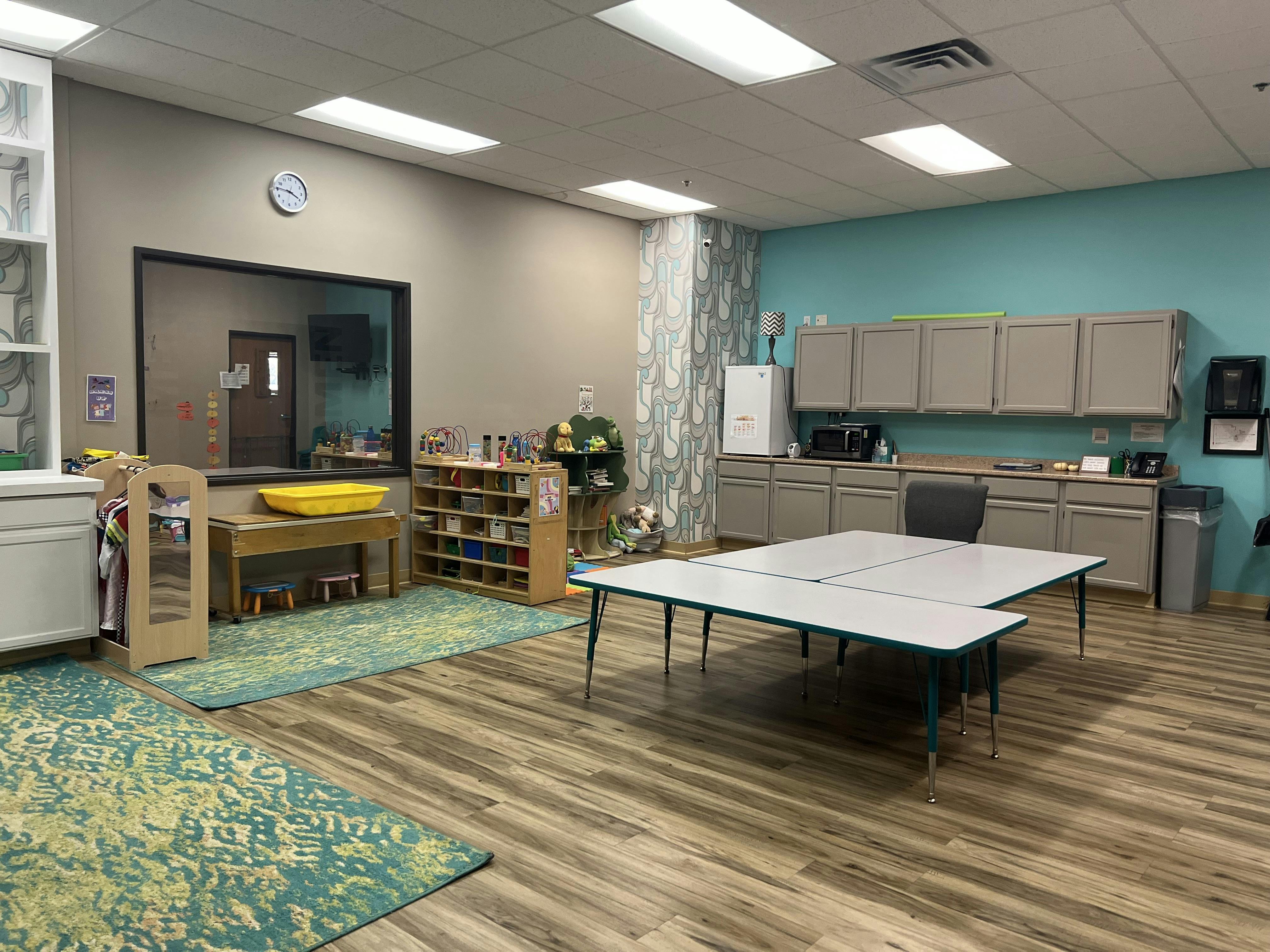 Classroom with tables, cabinets, and a window looking into another room