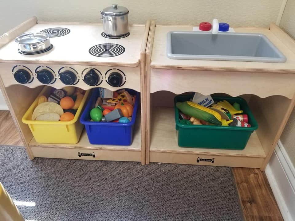 Play kitchen with stove, sink, and bins of toy food