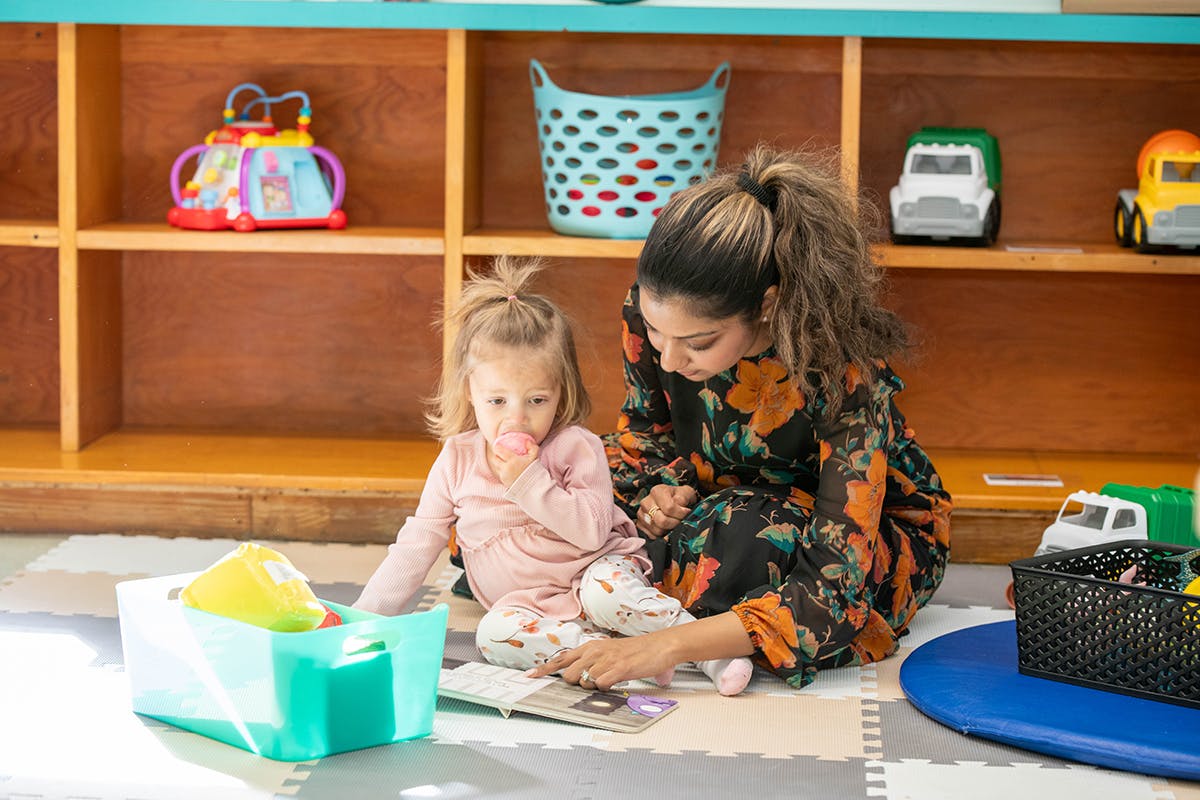 Adult and child sitting on floor reading a book in a classroom