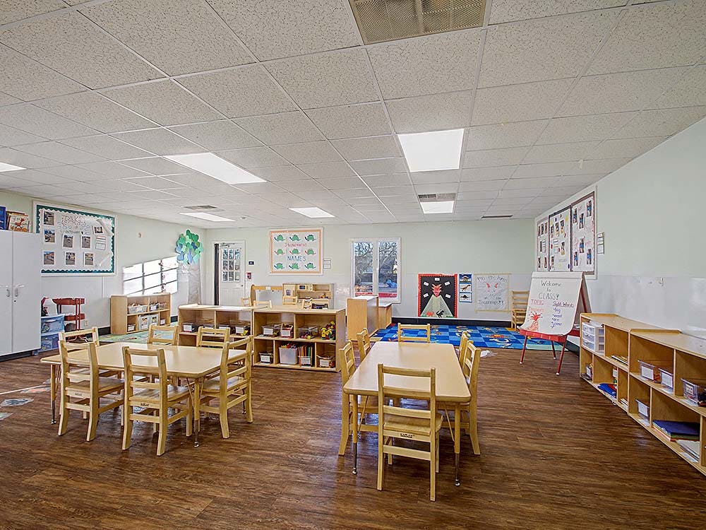 Empty classroom with small wooden tables and chairs on a wooden floor
