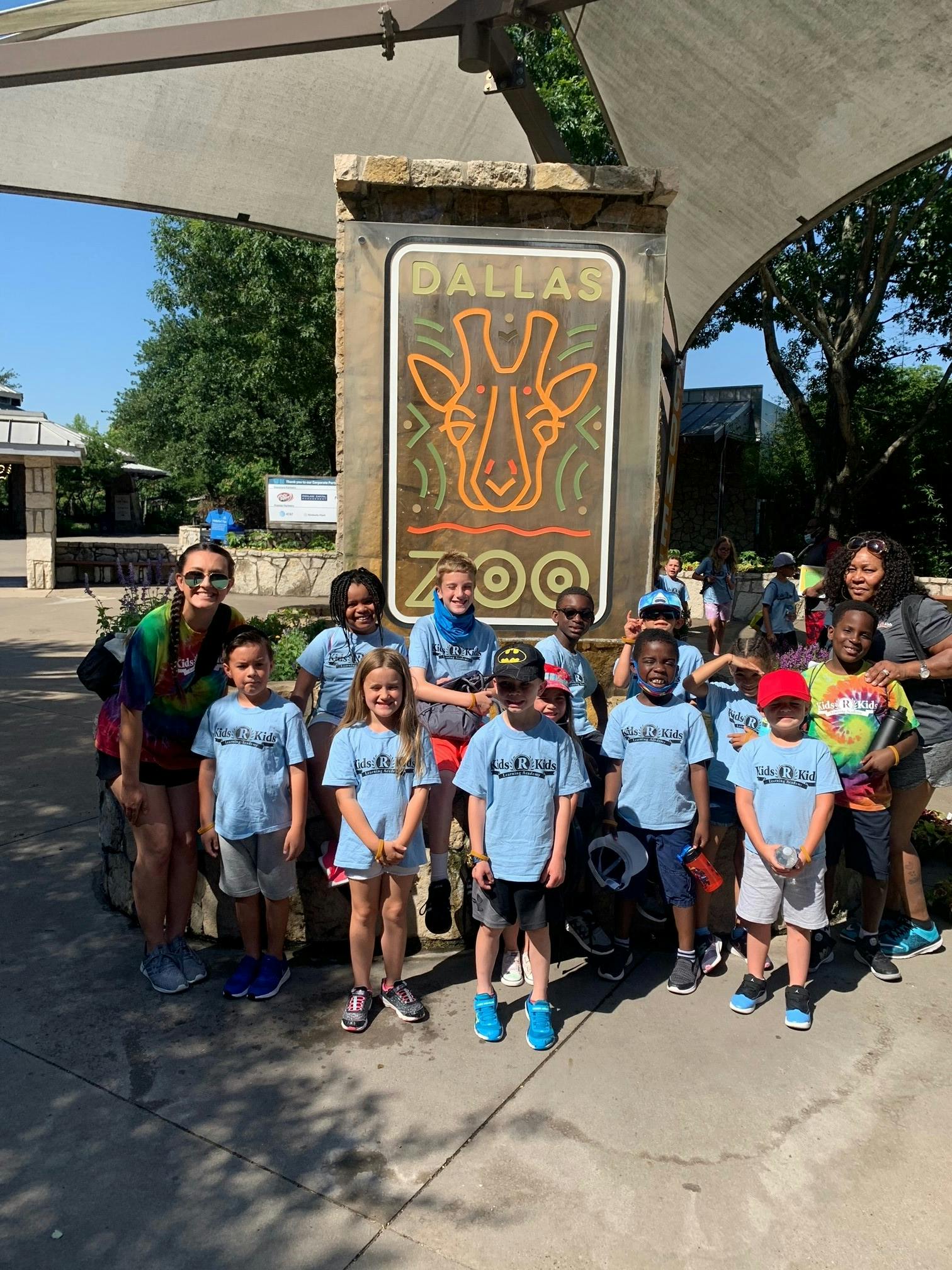 Group of adults and children posing in front of a Dallas Zoo sign