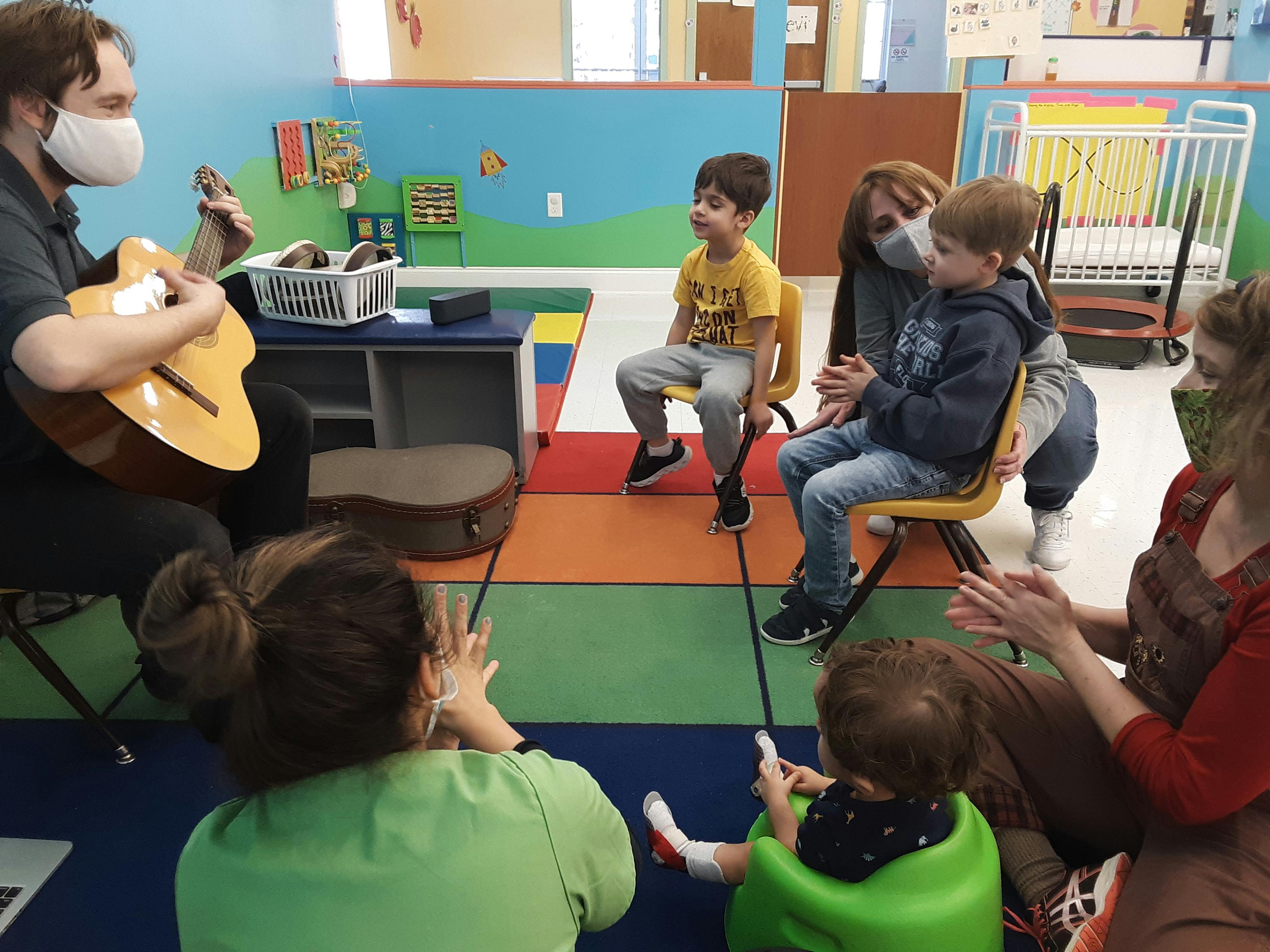 Person playing guitar for children and adults in a classroom