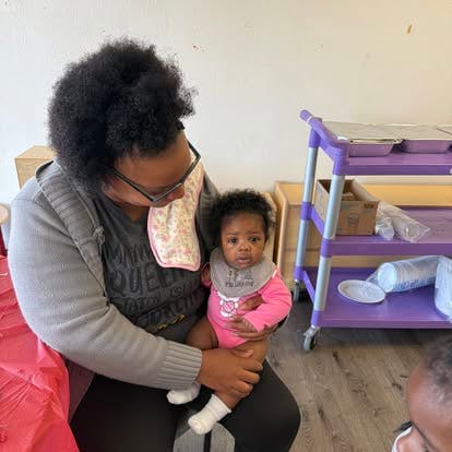 Person holding an infant wearing a pink outfit and gray bib