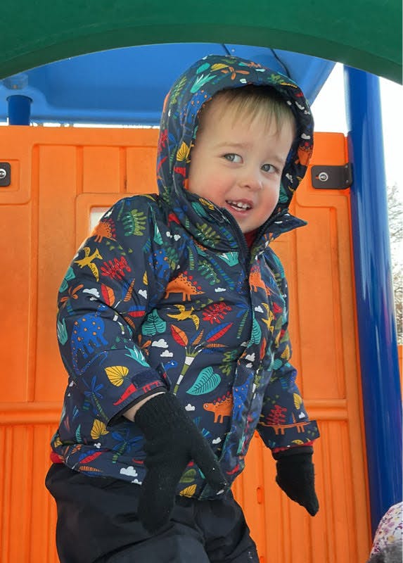 Child in a dinosaur print winter coat and mittens