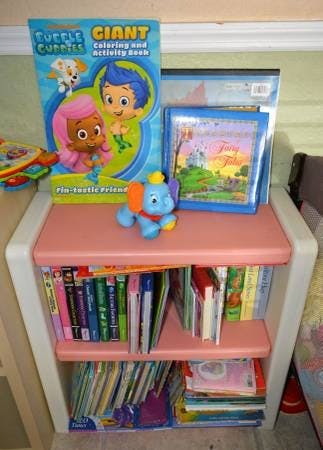 Children's books and a toy elephant on a small pink bookshelf