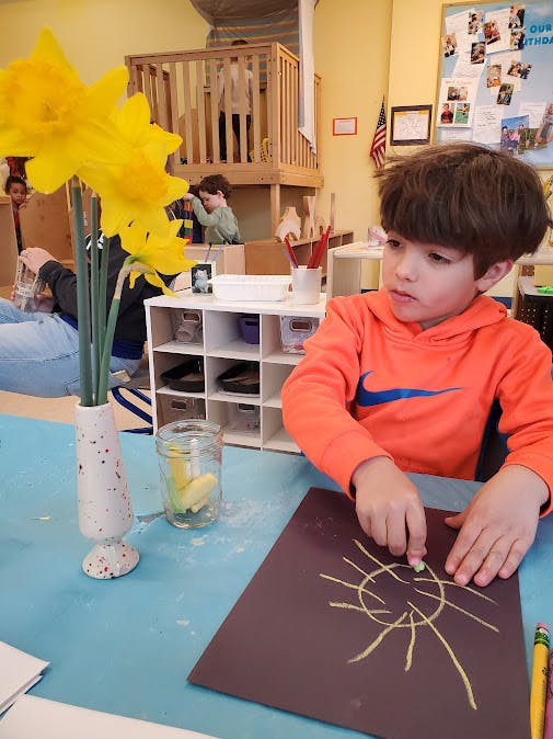 Child drawing a sun on dark paper with chalk in a classroom