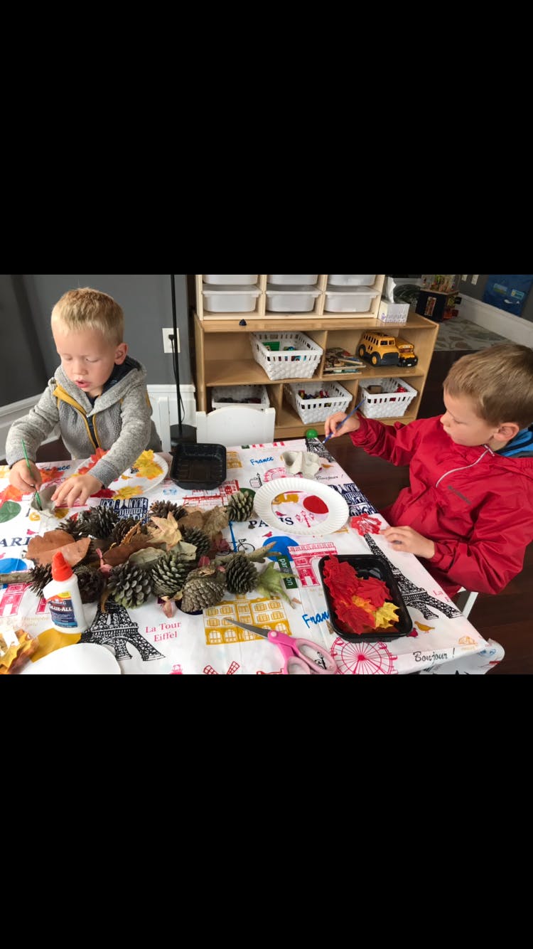 Two children doing crafts at a table with pinecones and glue