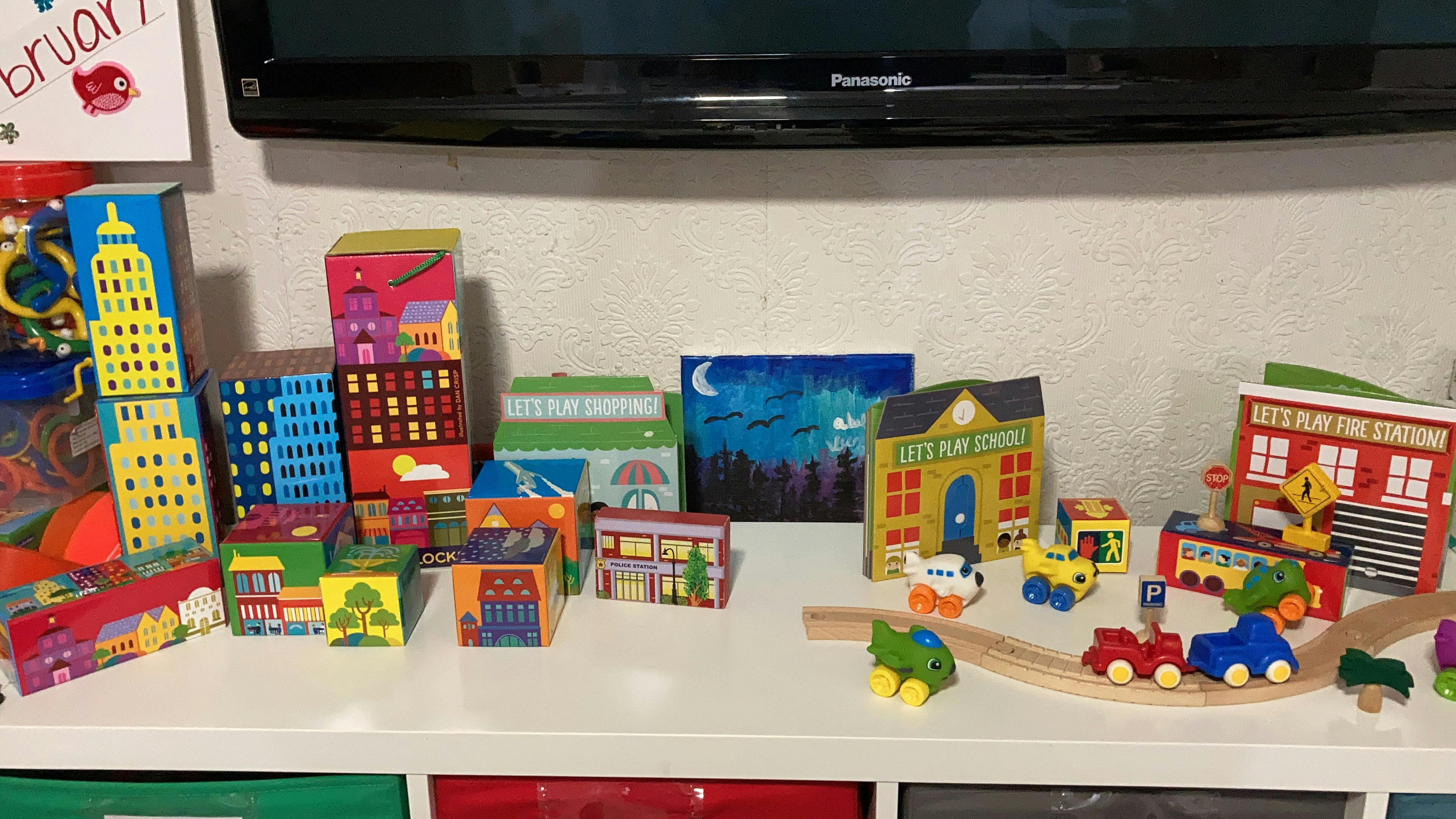 Toy city scene with buildings, vehicles, and a wooden train track