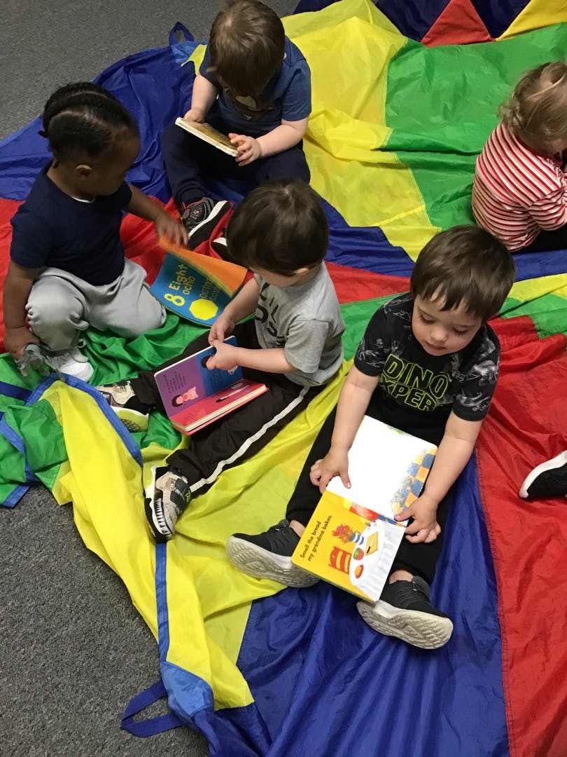 Children sitting on a colorful parachute reading books