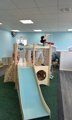 Child standing on top of a wooden play structure with a slide