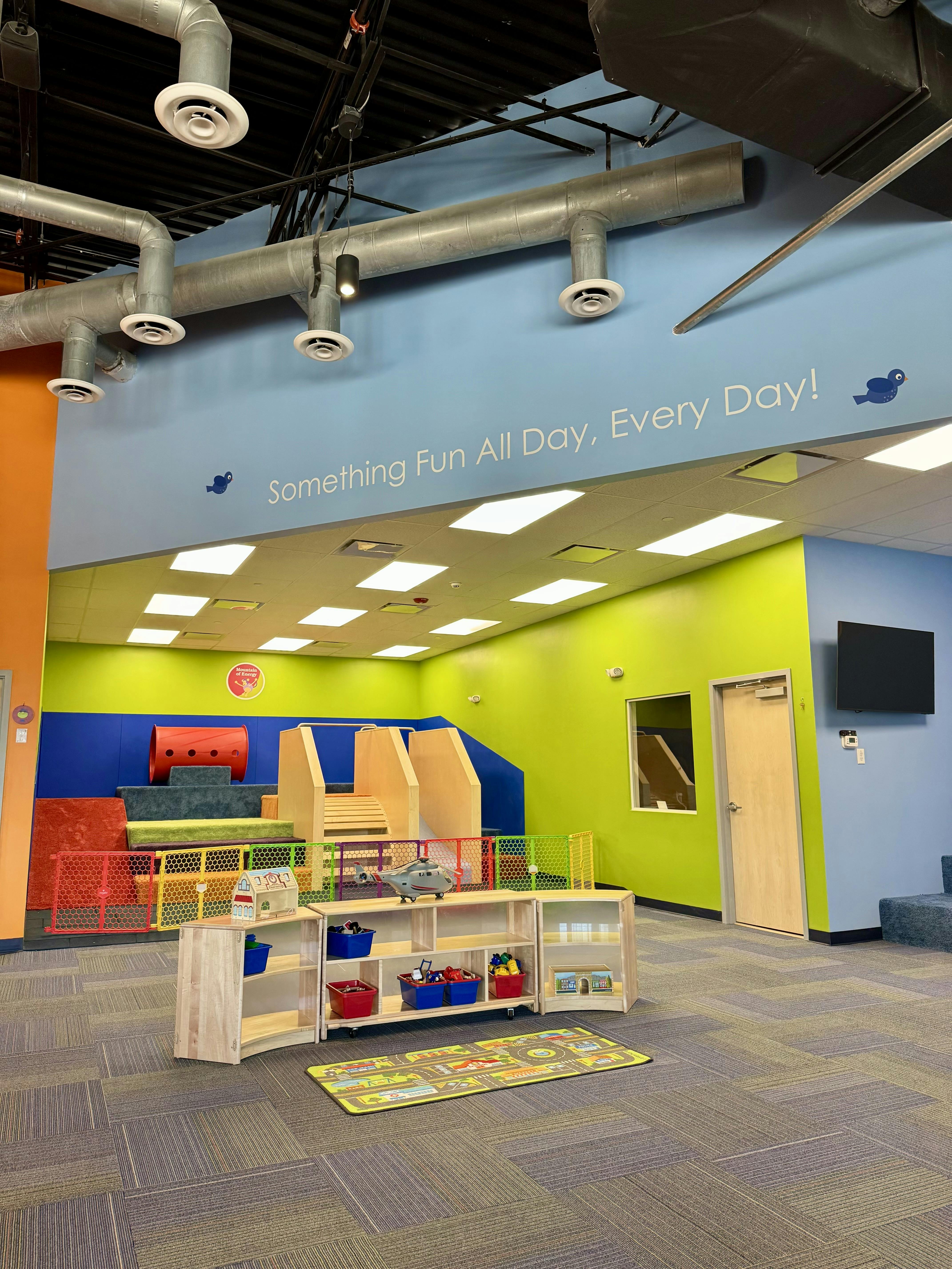 Indoor play area with soft play structures, shelving with toys, and blue and green walls