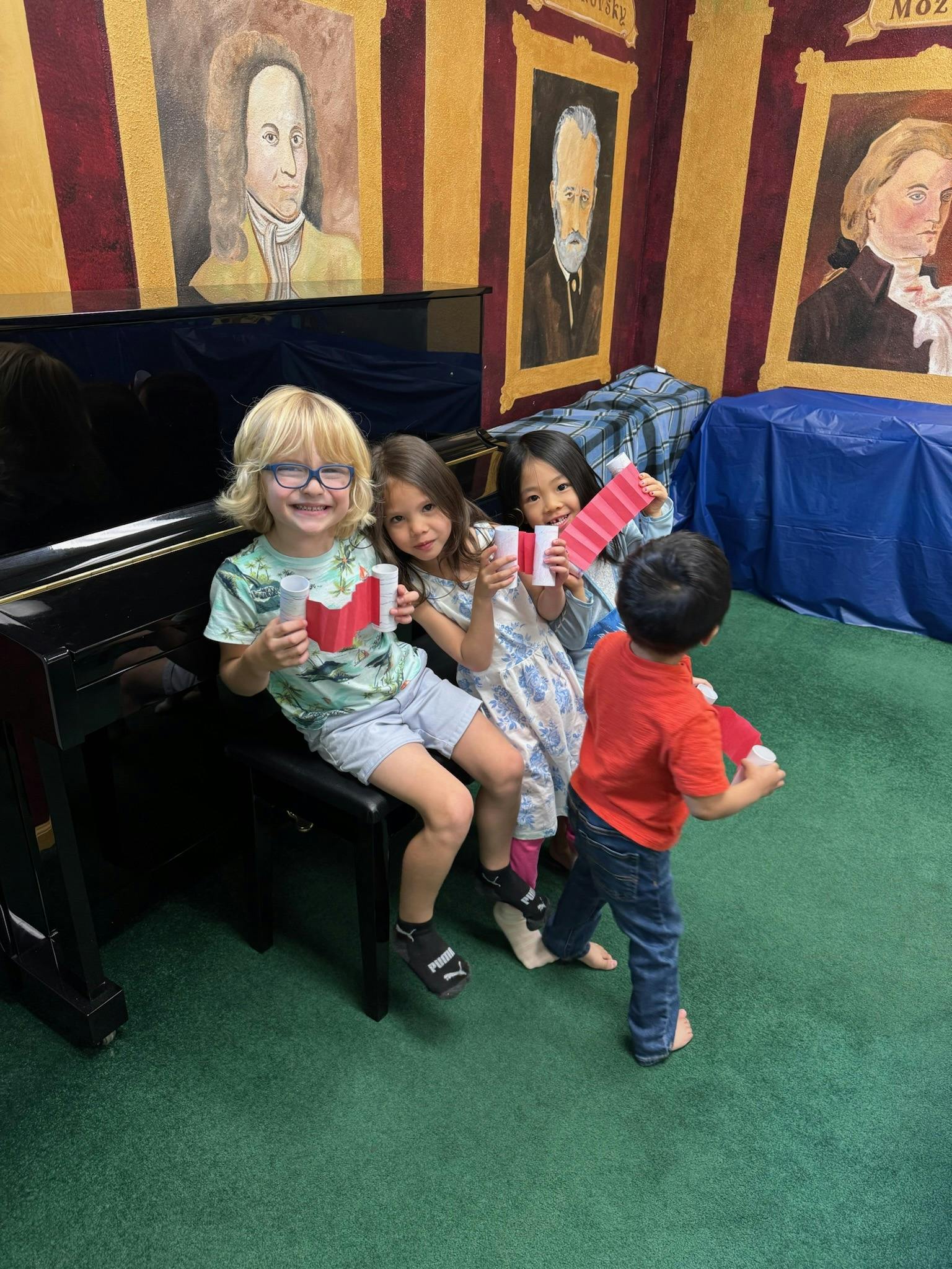 Three children holding paper crafts while sitting on a piano bench